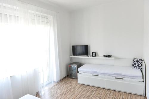 a white bedroom with a bed and a tv at Élmény Balaton Hotel in Alsóörs