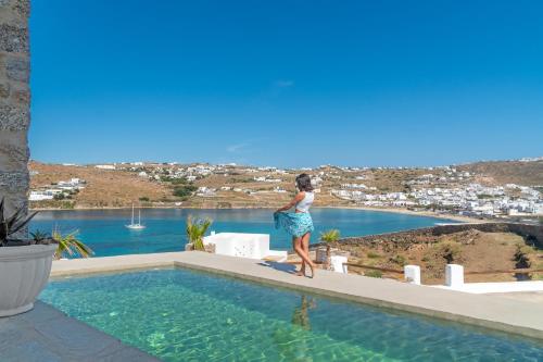 a woman standing on the edge of a swimming pool at CORFOS BLUE MYKONOS in Ornos