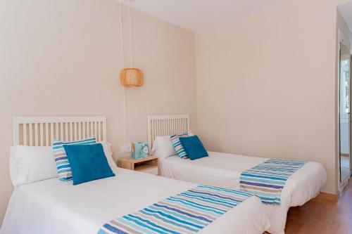 two beds in a white room with blue pillows at Hotel Aubí in Sant Antoni de Calonge