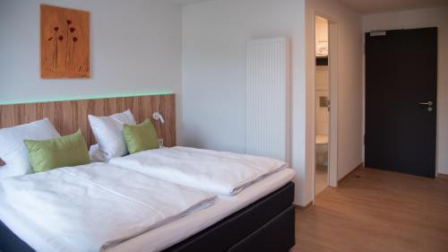 um quarto com uma cama com lençóis brancos e almofadas verdes em Gasthof zur Post em Lalling