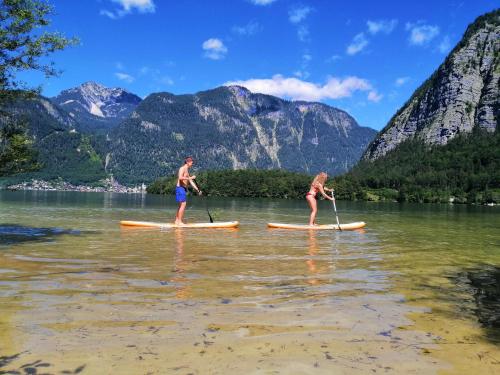 two people on paddle boards on a lake with mountains at Dormio Hotel Obertraun in Obertraun