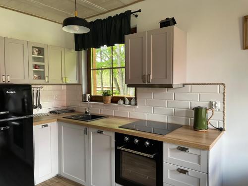 a kitchen with white cabinets and a black refrigerator at Domek Pod Lasem 45,1 Ostoja Bukowo in Borowy Młyn