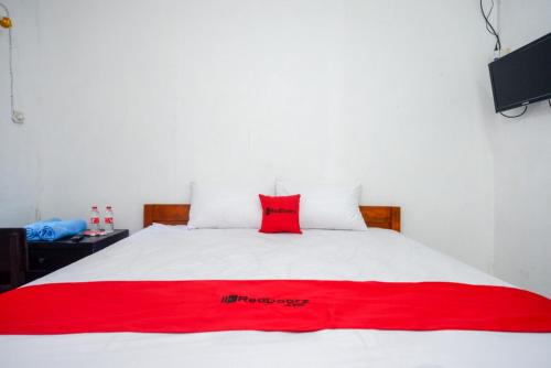 a red pillow sitting on top of a white bed at RedDoorz Syariah @ Ndalem Kembang Sore Yogyakarta in Timuran