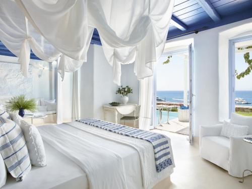 a white bedroom with a bed and a view of the ocean at Mykonos Blu, Grecotel Boutique Resort in Psarou