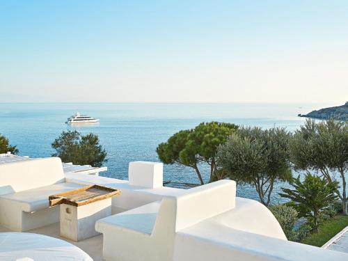 a beach area with chairs, tables and umbrellas at Mykonos Blu, Grecotel Boutique Resort in Psarou