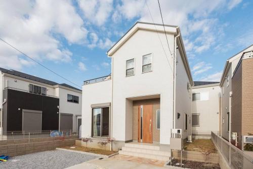 une maison blanche avec une porte marron dans l'établissement ゆうゆう布佐駅新築戸建Free Wifi, à Abiko