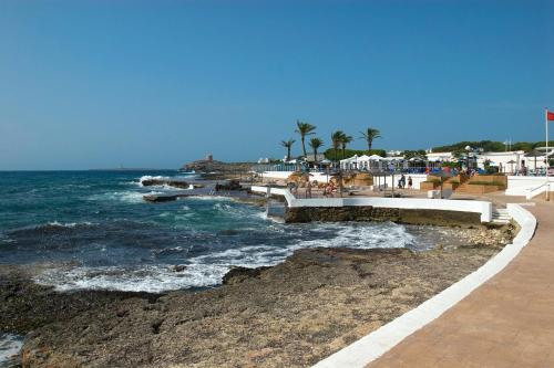 a beach with the ocean and buildings and palm trees at Villa Mencia by Villa Plus in S'Algar