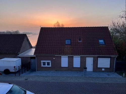 una casa con techo y puesta de sol en el fondo en Comfortabele woning mét omheinde tuin aan water voor 12 p, en Oostburg