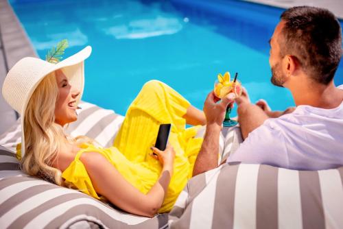 a man and a woman sitting on a beach chairs by a swimming pool at Lielupe Hotel SPA & Conferences by Semarah in Jūrmala