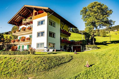 a large house on a hill with a girl in the grass at Haus Lohengrin Ferienwohnung 4 in Siusi