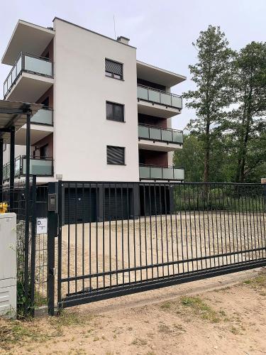 a white building with a fence in front of it at Apartament SZAFIROWA MIERZEJA w Unieściu- 365PAM in Unieście