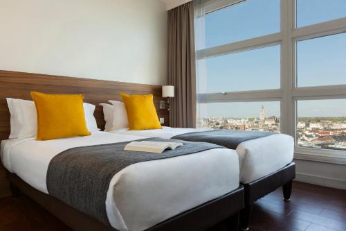 a bedroom with a large bed with yellow pillows and a window at Citadines City Centre Lille in Lille
