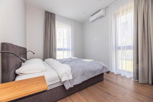 a white bedroom with a bed and two windows at Sunset Apartment at Sventosios Vartai in Palanga