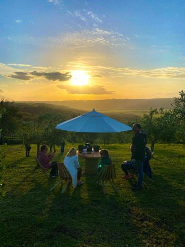 a group of people sitting around a table under an umbrella at Pousada Olival Vila do Segredo in Caçapava do Sul