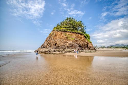 a group of people walking on a beach with a large rock at Beach Captain - Meredith Lodging in Neskowin
