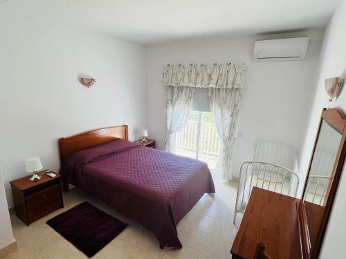 1 dormitorio con cama morada y ventana en Vila Flora, en Santa Bárbara de Nexe