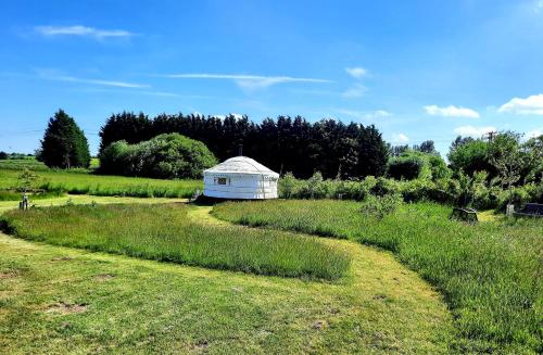 a field with a white building in the middle at Cranfield Retreat & Glamping in Long Melford