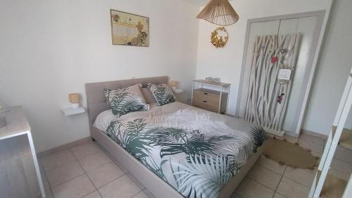 um pequeno quarto com uma cama com lençóis estampados de palmeira em Gite chaleureux pour deux avec jacuzzi ou piscine selon dates em Graveson