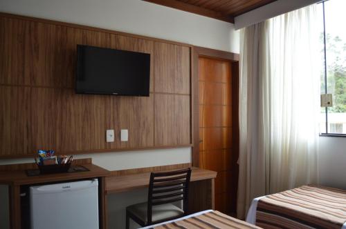 a hotel room with a desk and a television on a wall at Pousada Terê Parque in Teresópolis