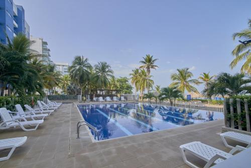 una piscina con sillas blancas y palmeras en Magico Apartamento Frente al Mar 3 Habitaciones PAZ282, en Coveñas