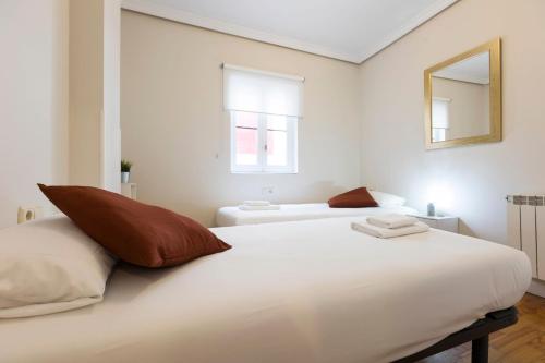 ein weißes Schlafzimmer mit 2 Betten und einem Spiegel in der Unterkunft Pensión Txoko Goxoa in Hondarribia