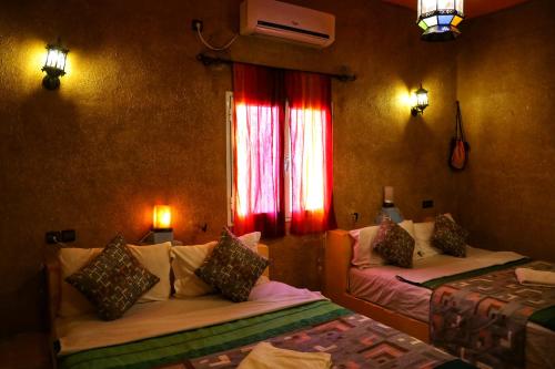 a room with two beds and a window with red curtains at Kasbah Du Berger & Piscine in Merzouga