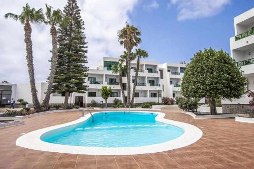 a swimming pool in front of a building with palm trees at Holyhome premium 106 in Costa Teguise