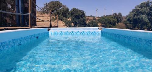 a pool of blue water with trees in the background at Casas de Campo do Castro da Cola in Marchicão