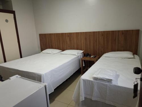 two beds in a hotel room with a table at Hotel Oscar Econômico Montes Claros in Montes Claros