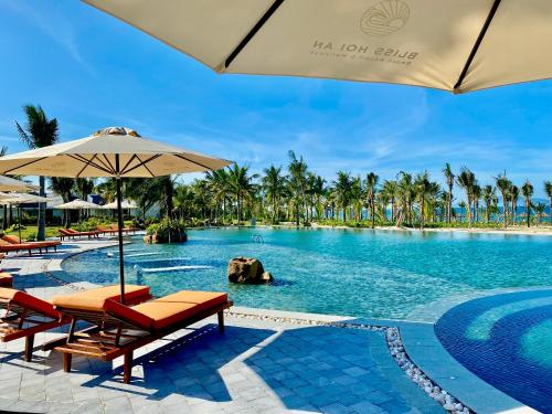 ein Pool in einem Resort mit Stühlen und einem Sonnenschirm in der Unterkunft Bliss Hoi An Beach Resort & Wellness in Hoi An
