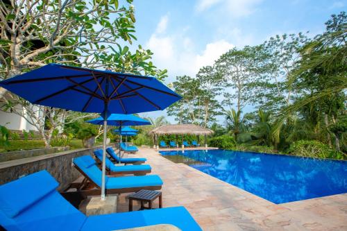 a pool with blue lounge chairs and umbrellas at Niyagama House in Galle