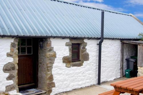 a white cottage with a metal roof and a wooden door at Deveron Valley Cottages in Marnoch