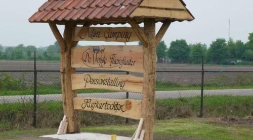 a wooden structure with signs on it in a field at Camping Amable in Someren-Heide