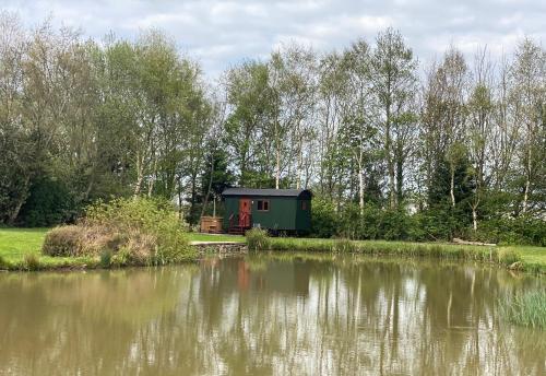 a green cabin next to a body of water at Heywood Glamping in Ormskirk