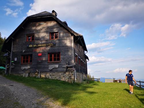 a woman walking in front of an old wooden building at Mountain Lodge Smrekovc in Šoštanj