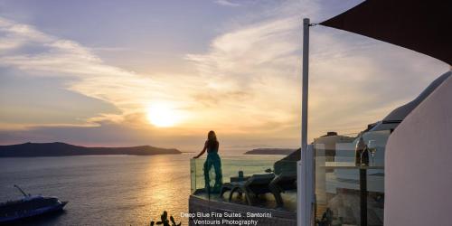 a woman standing on a balcony watching the sunset at Fira Deep Blue Suites in Fira