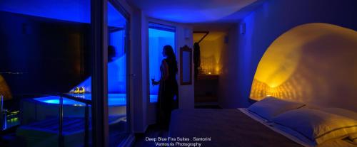 a person standing in a room with a bed and a window at Fira Deep Blue Suites in Fira