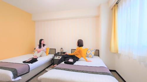 two women sitting on beds in a room at Hotel Area One Oita in Oita