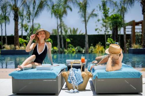 two women sitting on beds next to a pool at Amanti, MadeForTwo Hotels - Ayia Napa in Ayia Napa