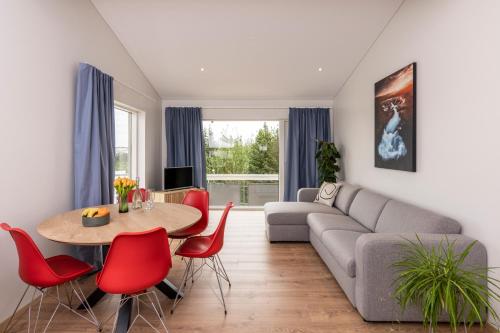 a living room with a couch and a table and red chairs at Lundur Apartments in Reykjavík