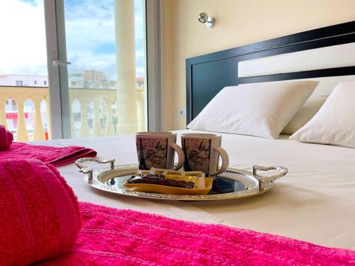 a tray with two mugs and cookies on a bed at Marku Palace in Ksamil