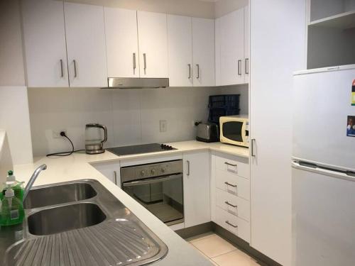 cocina con armarios blancos, fregadero y microondas en Merivale stay in South Brisbane two beds two baths one parking en Brisbane