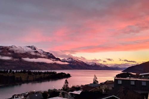 a sunset over a body of water with snow covered mountains at Lovely Apartment- Amazing Lake & Mountain Views in Queenstown