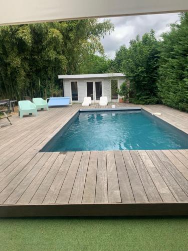 - une piscine avec une terrasse en bois et des chaises dans l'établissement Villa Marcel Spa Sauna Billard Piscine 25mn de Bordeaux, à Cérons