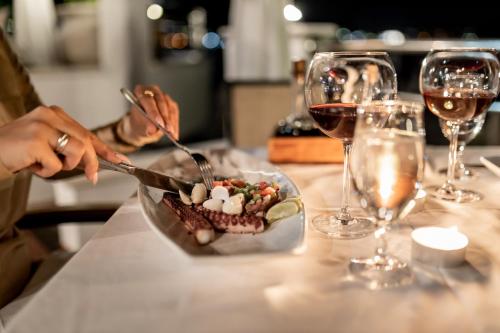 a person cutting a plate of food on a table with wine glasses at Hotel Perla in Herceg-Novi
