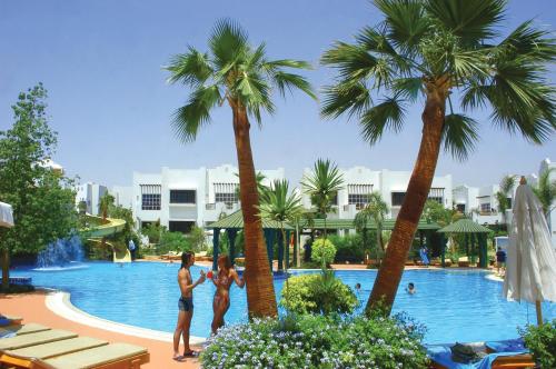 two women are standing in a swimming pool with palm trees at Herrmes Hostel in Sharm El Sheikh