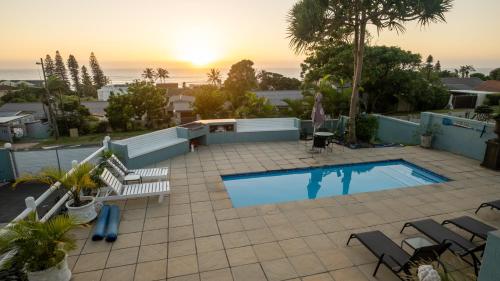 a swimming pool on a patio with chairs and a sunset at At The Sea Ballito in Ballito