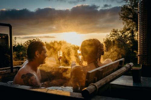 Un uomo e una donna in una vasca da bagno con il tramonto di Blatchford Briar - Award Winning Private Shephards Huts with their own Secluded Hot Tubs a Milton Abbot