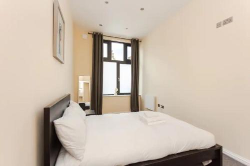 a bedroom with a bed with white sheets and a window at Stylish 2 Bedroom Apartment in Greenwich in London
