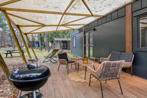 a patio with a bbq and chairs and a grill at Cosy 4 pers chalet midden in bos op de Veluwe in Doornspijk